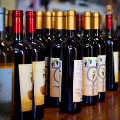 Rząd butelek wina, w tym wino regionalne, z etykietami w języku hebrajskim i grafiką winogron.