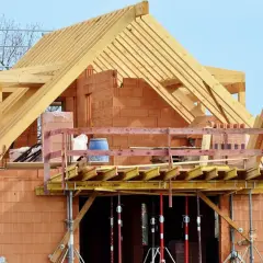 Budowa domu z cegły, widoczna drewniana konstrukcja dachu i balkon. Dopuszczalny błąd wymiarów budynku jest tu nieistotny, liczy się postęp prac.