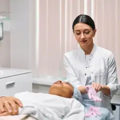 Kosmetikerin zieht Handschuhe an, während Kundin auf Liege liegt.