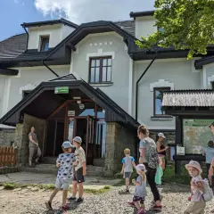 Rodzina przy schronisku na Magurce Wilkowickiej. Dzieci zwiedzają okolicę, a dorośli planują trasę na mapie.