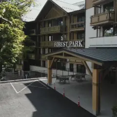 Elegancki hotel 5 gwiazdkowy Forest Park otoczony zielenią, z parkingiem i zadaszonym wejściem.