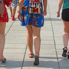 Trzy kobiety idą chodnikiem. Jedna ma na sobie czerwoną sukienkę w kwiaty, druga niebieską, a trzecia czarne szorty. Widać zaczerwienione obtarte uda u kobiety w czerwonej sukience.