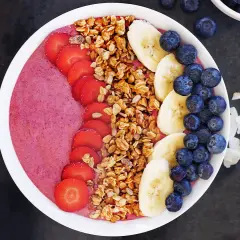En färgglad acai bowl med jordgubbar, banan, blåbär och granola. Serveras med mandlar och kokosflingor.