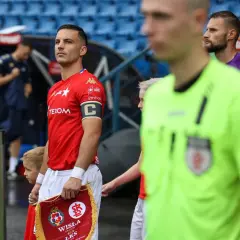 Piłkarz Wisły Kraków z kapitańską opaską, który awansował do ekstraklasy w piłce nożnej, trzyma flagę.