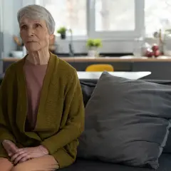 Starsza kobieta siedzi na kanapie, zastanawiając się, jak zostać opiekunem osoby niepełnosprawnej dorosłej.