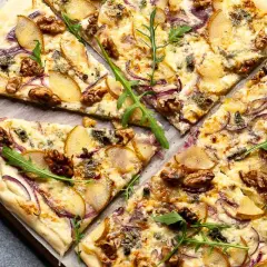 Ein köstlicher flammkuchen vegetarisch mit Birnenspalten, roten Zwiebeln, Walnüssen und Rucola.