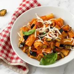 Un plato de pasta alla norma con berenjenas fritas, salsa de tomate y queso rallado, decorado con albahaca fresca.