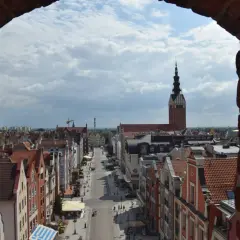 Widok na ulicę i kamienice w **starym mieście Elbląg**. W oddali widać wieżę kościoła.