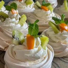 Pyszne gniazdka bezowe z kremem mascarpone, ozdobione kawałkami kiwi, pomarańczy i listkami mięty.