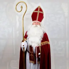 Mężczyzna w stroju św. Mikołaja biskupa, z białą brodą, mitrą i pastorałem, trzyma książkę.