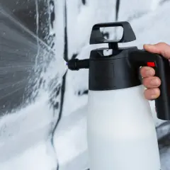 Mano che spruzza schiuma per lavare auto a casa con un'idropulitrice.