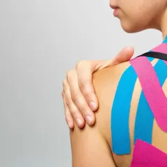 Kobieta z kolorowymi taśmami na ramieniu i plecach. To przykład, co to jest kinesiotaping, metoda wspierająca mięśnie i stawy.