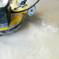 Eine Poliermaschine bearbeitet einen geschliffenen Betonboden, hinterlässt feinen Staub und glatte Spuren.