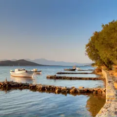 Bateaux blancs et bleus ancrés dans une baie paisible, avec des collines en arrière-plan, évoquant la sérénité de l'ile Crete.