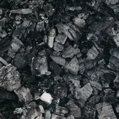 Gros plan sur des morceaux de machefer pellet, résidus noirs et gris de combustion, évoquant la chaleur d'un feu de bois.