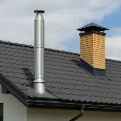 Nowy montaż komina systemowego na zewnątrz domu, obok tradycyjnego, ceglanego komina.
