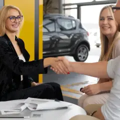Uśmiechnięta para zawiera umowę cesji leasingu z doradcą w salonie samochodowym.