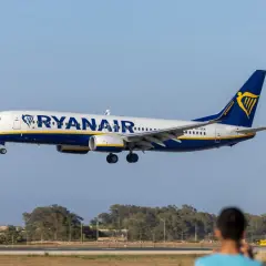 Samolot Ryanair lądujący na tle nieba i drzew.