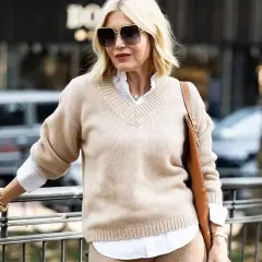 Elegancka kobieta po 50-tce w beżowym swetrze i białej koszuli. Stylowa moda dla 50 latki.