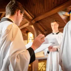 Jeunes hommes en surplis, se préparant pour un baptême protestant. L'un lit un texte, l'autre écoute attentivement.