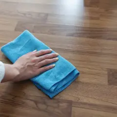 Mano con panno blu che pulisce un pavimento in legno, mostrando come togliere la colla dal legno con delicatezza.