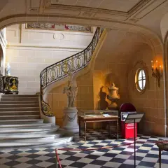Escalier majestueux du musée Nissim de Camondo, avec sa rampe dorée, sa statue et son sol à damier.