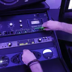 Main d'un ingénieur du son ajustant les potentiomètres d'un rack d'équipement audio, en pleine action de mastering musique.