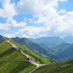 Szlak turystyczny na Kasprowy Wierch w Tatrach. Zielone zbocza, kamienna ścieżka i piękne, błękitne niebo z chmurami.