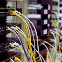Faisceau de câblage RJ45 b, avec des câbles blancs, jaunes et gris connectés à des commutateurs réseau empilés.