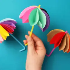 Bunte Papier-Regenschirme, die zum **Regenschirm basteln einfach** einladen. Ein gelber Strohhalm hält einen bunten Schirm.