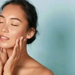 Donna con pelle luminosa e mani sul viso, un esempio di perché i coreani hanno la pelle perfetta.