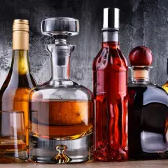 Karafka i butelki z bursztynowym płynem, być może wyśmienity brandy, stoją na drewnianym blacie.