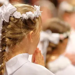 Dziewczynka w białej sukience i wianku modli się. To piękny widok, co na komunie.