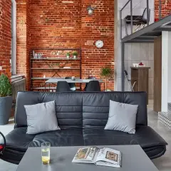 Nowoczesne wnętrze loftowe z ceglaną ścianą, czarną kanapą i metalowymi schodami.