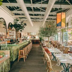Ambiance chic au Perchoir Porte de Versailles : bar animé, tables dressées, oliviers et végétation luxuriante pour un repas en terrasse.