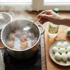 Une main ajoute du vinaigre blanc dans l'eau bouillante où cuisent des œufs. C'est une astuce pour éviter que les œufs durs ne se fendent.