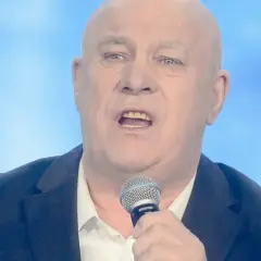 Ryszard Rynkowski śpiewa, trzymając mikrofon. Jego charakterystyczne utwory poruszają serca słuchaczy.