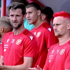 Piłkarze Widzewa Łódź w czerwonych koszulkach, jeden z nich ma jaskrawo-czerwone włosy.