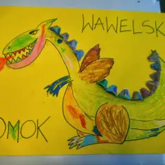 Kolorowa praca plastyczna przedstawiająca zielonego smoka wawelskiego ziejącego ogniem. Napisy "SMOK" i "WAWELSKI" dopełniają dzieło.