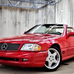 Czerwony kabriolet Mercedes-Benz SL500 z beżowym wnętrzem, zaparkowany przy betonowej ścianie.