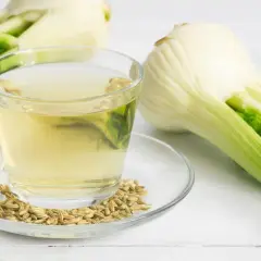Una tazza di tisana al finocchio, semi di finocchio e bulbi freschi su uno sfondo bianco.