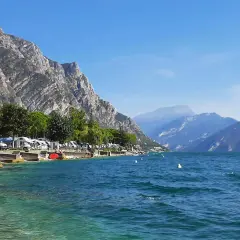 Malowniczy widok na jezioro Garda z campingiem, kamienistym brzegiem i górami w tle. Idealne miejsce na wakacje.