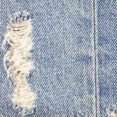 Zbliżenie na niebieski denim z przetarciami. Dowiedz się, jak zrobic przetarcia na dzinsach, by nadać im stylowy, znoszony wygląd.