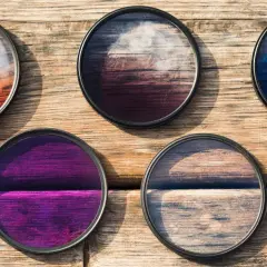 Five circular camera filters with colorful gradients, perfect for telephoto photography, lie on a wooden surface.