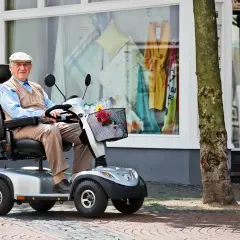 Älterer Herr im elektrischen Rollstuhl vor einem Schaufenster. Dank der Krankenkasse kann er mobil bleiben.