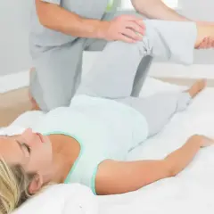 Fizjoterapeuta wykonuje test Patricka na leżącej kobiecie, delikatnie unosząc jej nogę.