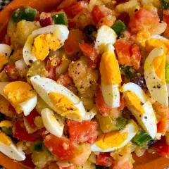 Ensalada campera con patatas, huevos duros, tomate, pimiento y aceitunas negras, todo mezclado y sazonado.