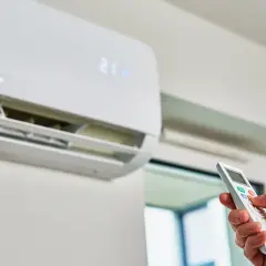 Mano con mando a distancia ajustando el aire acondicionado, que muestra el símbolo calefacción y la temperatura de 21 grados.