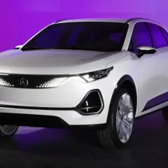 Białe, nowoczesne polskie auto elektryczne z futurystycznymi światłami LED, prezentowane na tle fioletowej ściany.