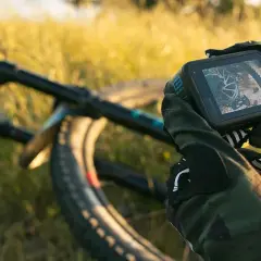 Ręce w rękawicach trzymają kamerę GoPro, gotową do nagrywania zjazdów na rowerze górskim. Niesamowite gopro zdjęcia czekają!